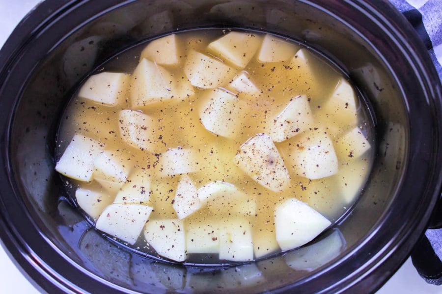 potato chunks in a slow cooker, covered with both and seasoning