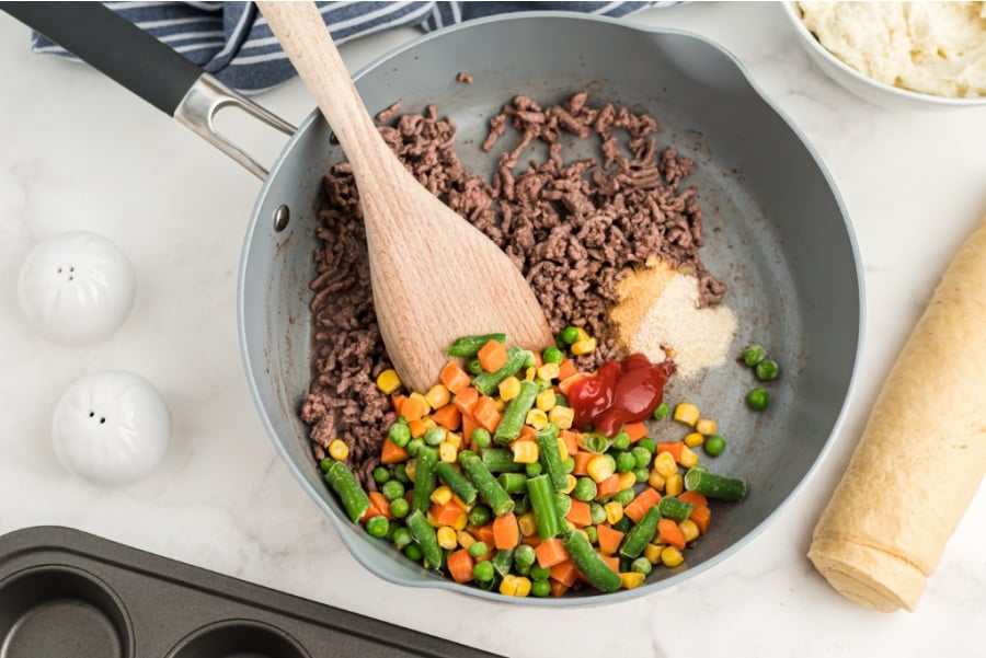 hamburger add garlic, ketchup, Worcestershire sauce, and frozen vegetables in a cooking pan with a wooden spoon stirring