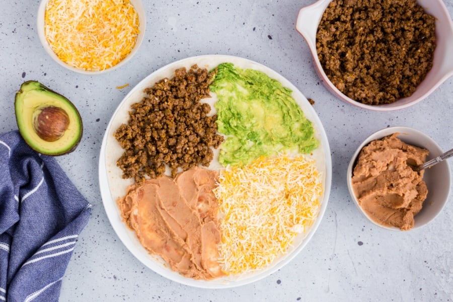 tortilla with beef, avocado, refried beans and cheese on top