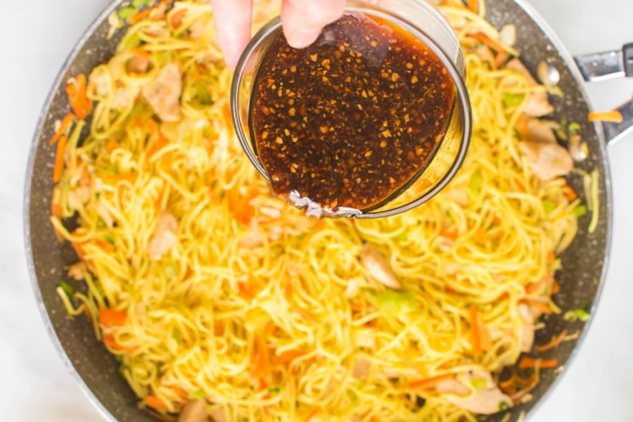 pouring sauce over noodles in a pan