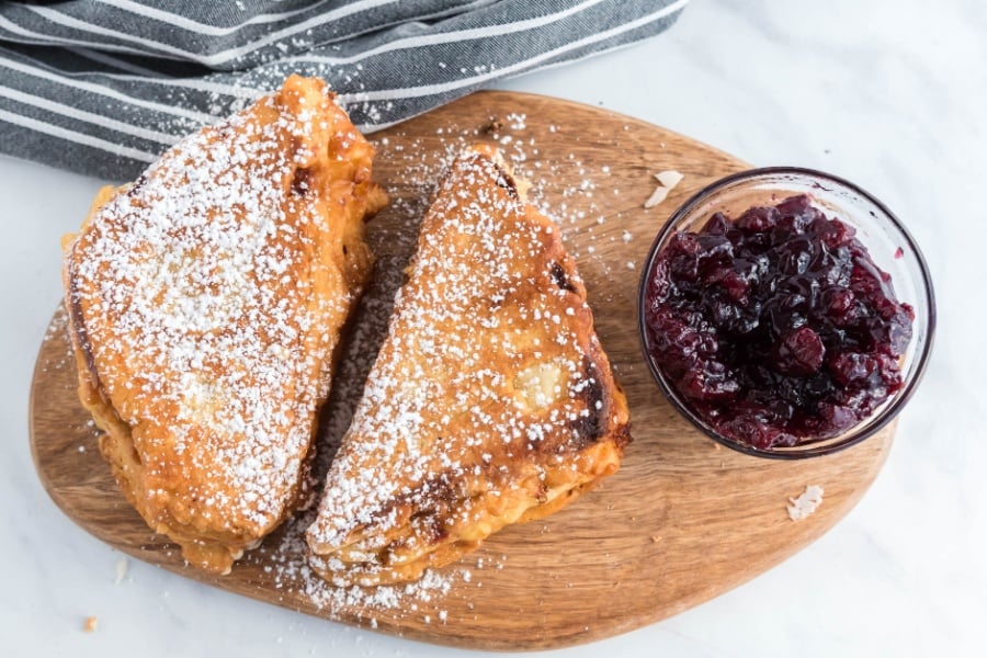 Monte Cristo sandwich on a cutting board with a bowl of jam
