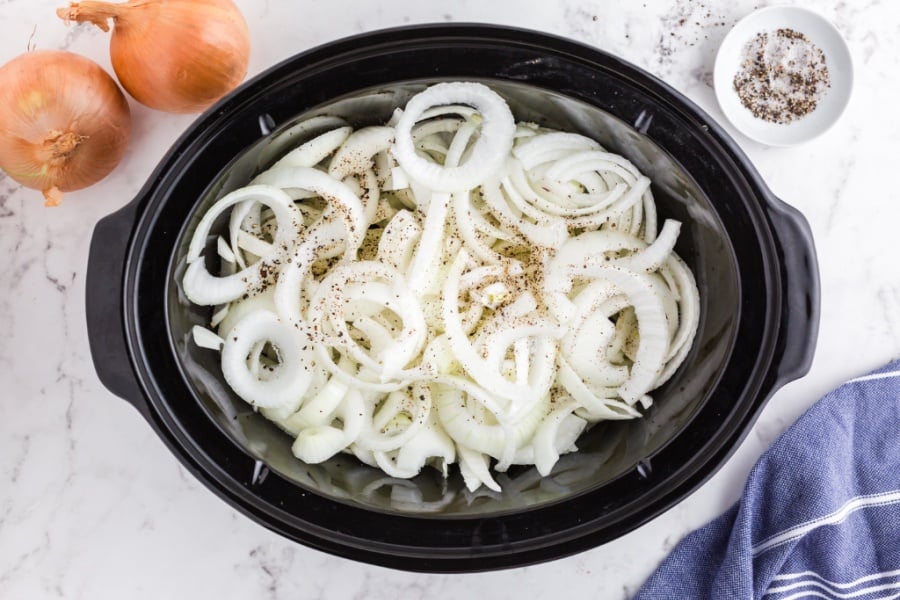 sliced onions and seasoning in a slow cooker