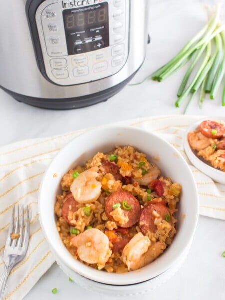 Jambalaya in a white bowl with pressure cooker in background