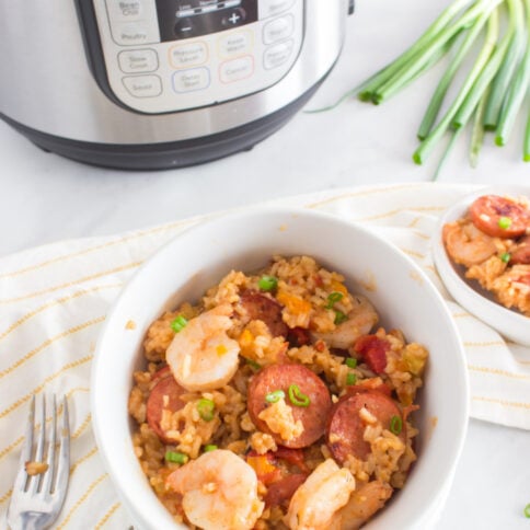 Jambalaya in a white bowl with pressure cooker in background