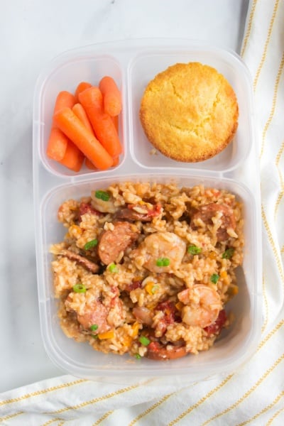 Jambalaya packed in a lunchbox with a muffin and baby carrots