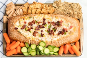 Mississippi Sin Dip in a bread loaf, surrounded by veggies and crackers