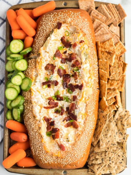 Mississippi Sin Dip in a bread loaf, surrounded by veggies and crackers