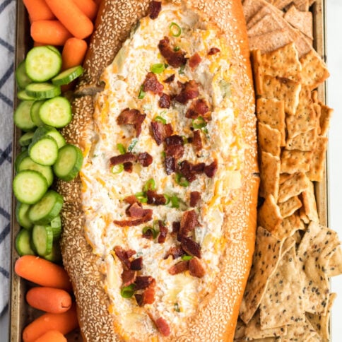 Mississippi Sin Dip in a bread loaf, surrounded by veggies and crackers