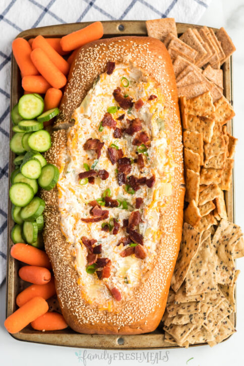 Mississippi Sin Dip in a bread loaf, surrounded by veggies and crackers