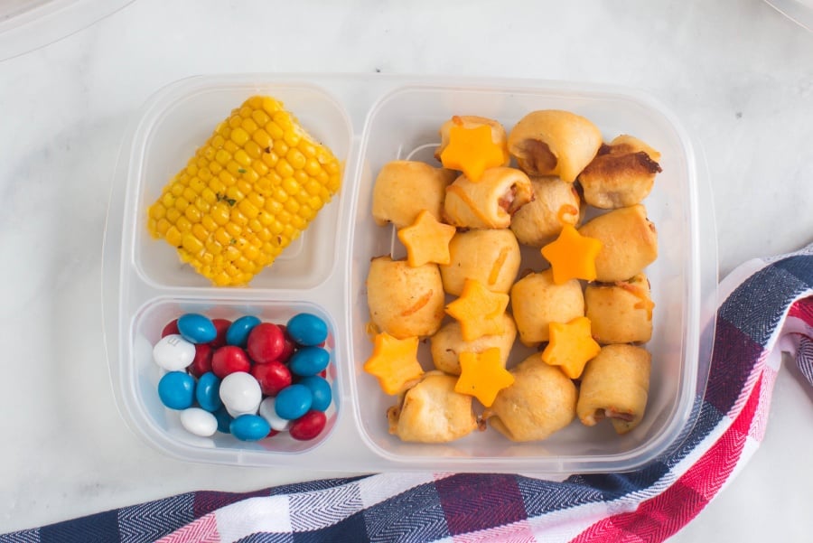 mini hotdogs, cheese stars, candies and corn on the cob in a lunchbox