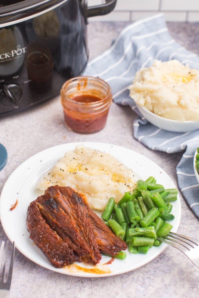 bbq brisket on a plate with green beans and mashed potatoes