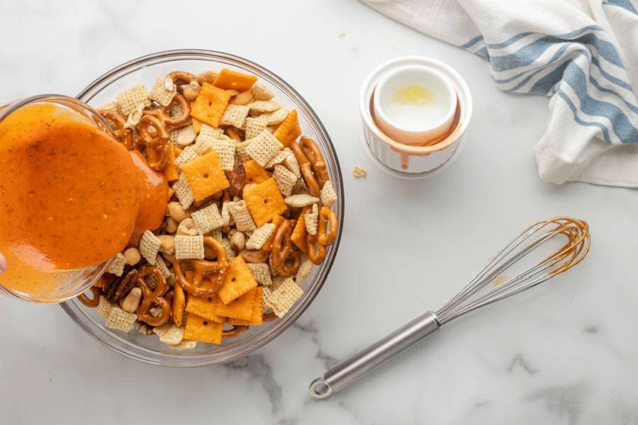 pouring buffalo mixture over chex mix