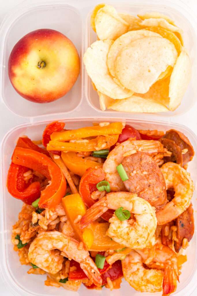 Jambalaya packed in a lunchbox with an apple and chips