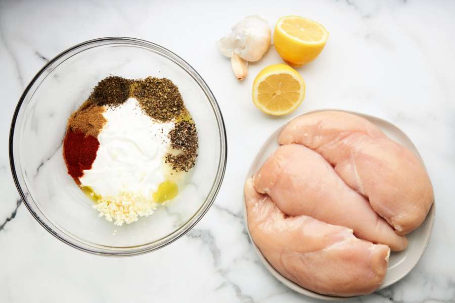 ingredients for marinade in a bowl and a plate of chicken breast