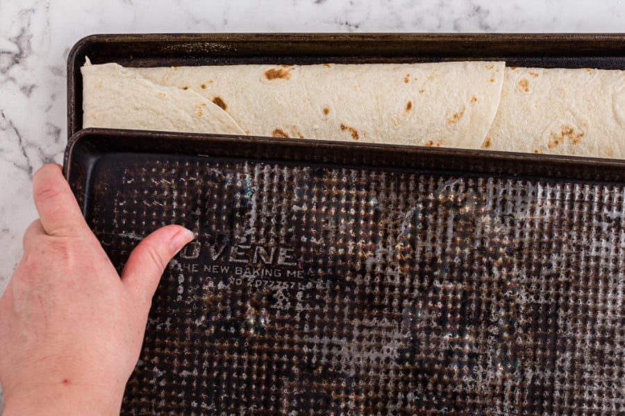 placing a second sheet pan on top of tortillas