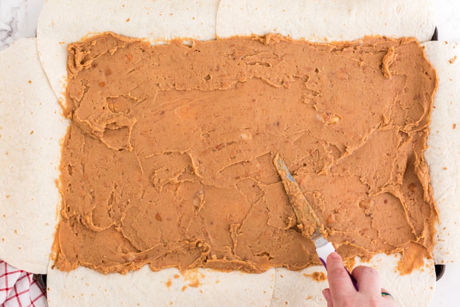 spreading refried beans on tortillas