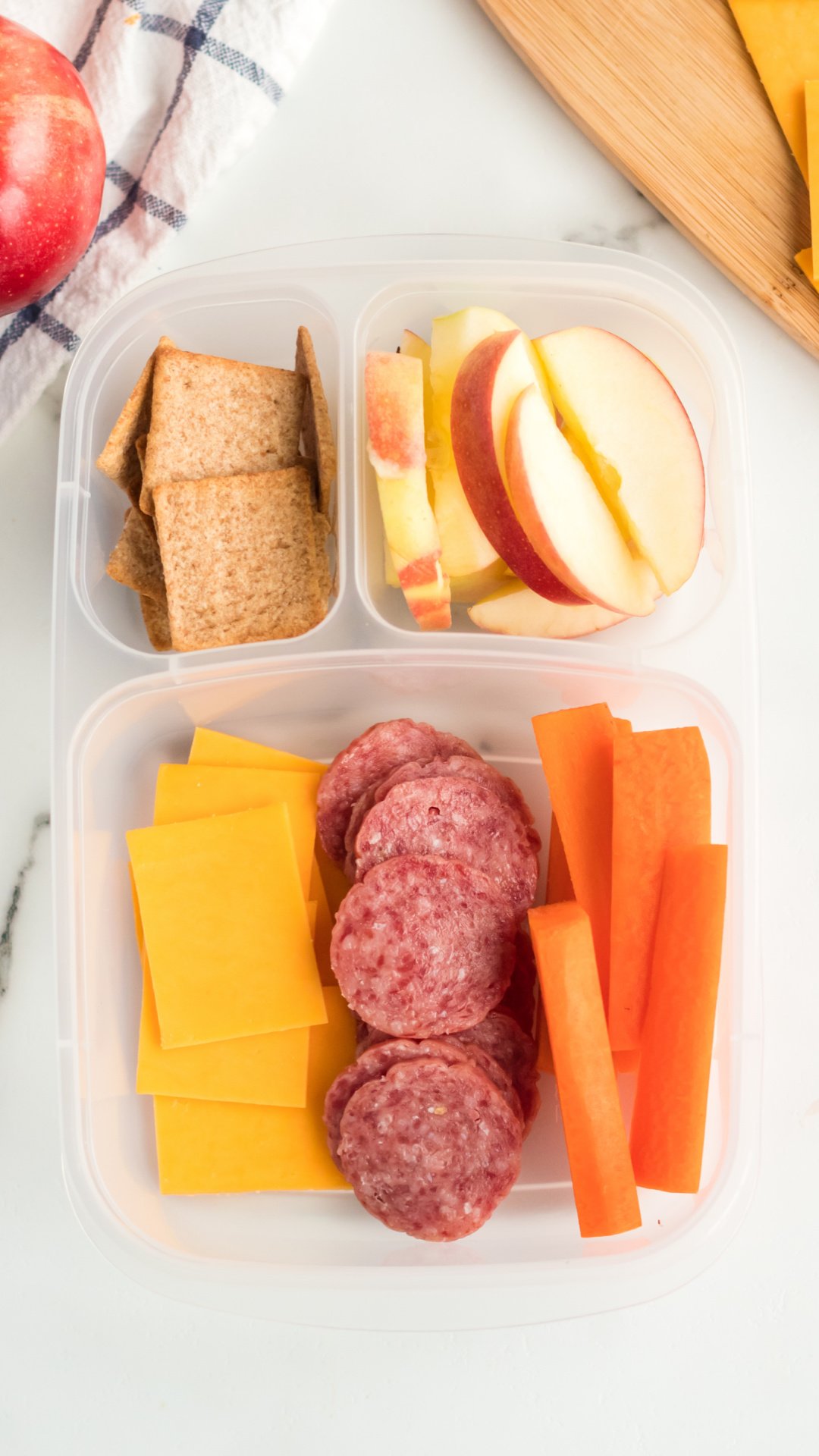 кутија за ручак са нарезаним сиром, саламом, шаргарепом, јабукама и крекерима