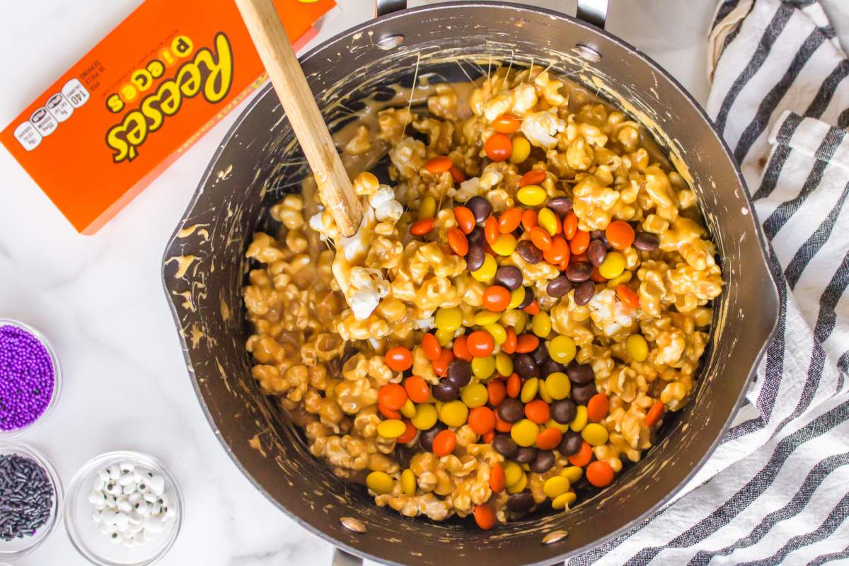 mixing in reeses pieces candy into popcorn mixture