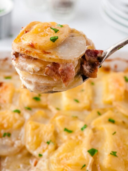 cheesy scalloped potatoes with bacon being scooped up with a spoon
