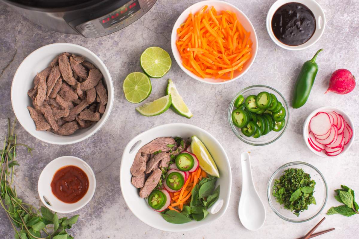 Instant Pot Beef Pho soup in bowl  with small bowls of toppings