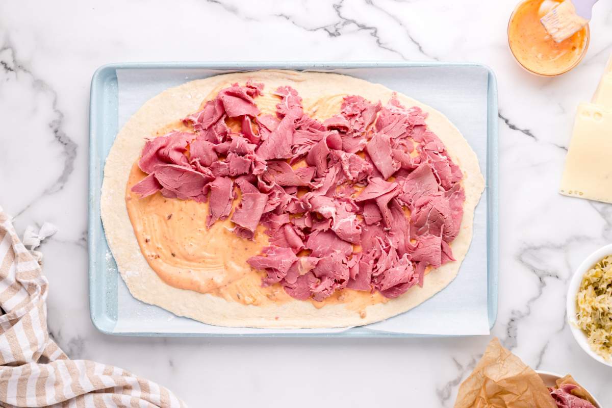 adding dressing and corned beef to pizza dough