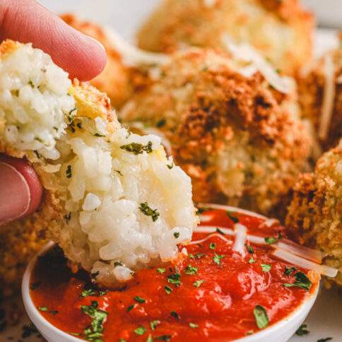 Air Fryer Arancini Rice Balls being dipped into red sauce