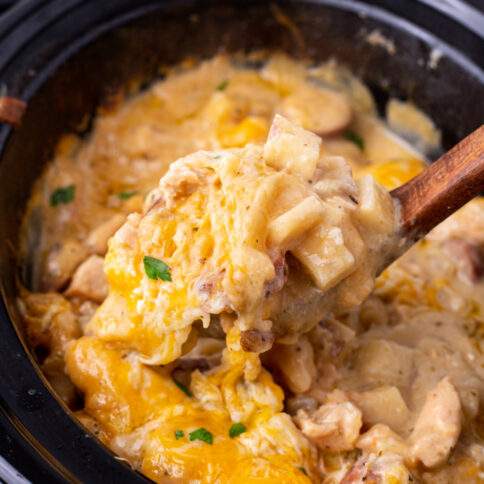 Crockpot Cheesy Chicken, Sausage, and Potato Casserole being scooped out of slow cooker