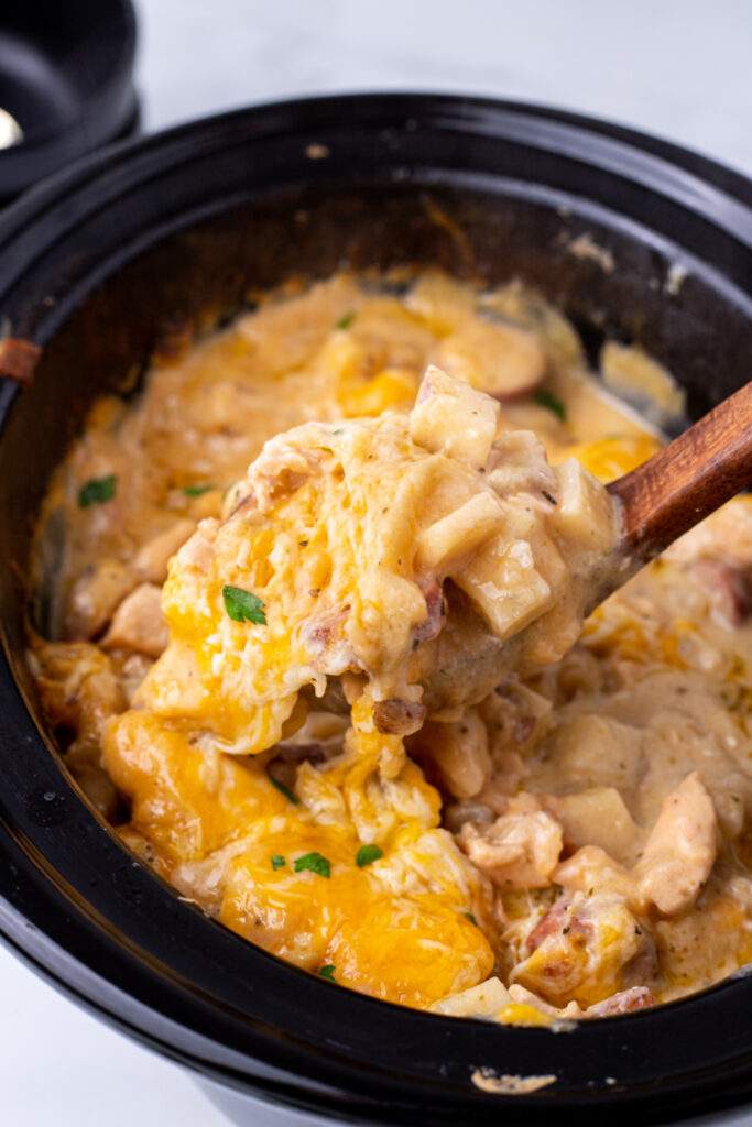 Crockpot Cheesy Chicken, Sausage, and Potato Casserole being scooped out of slow cooker