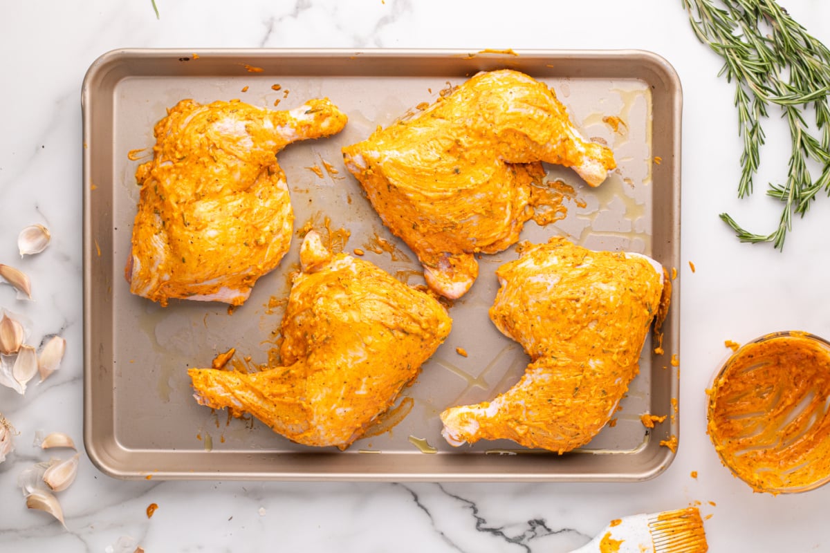 chicken quarters on baking sheet topped with seasoning butter