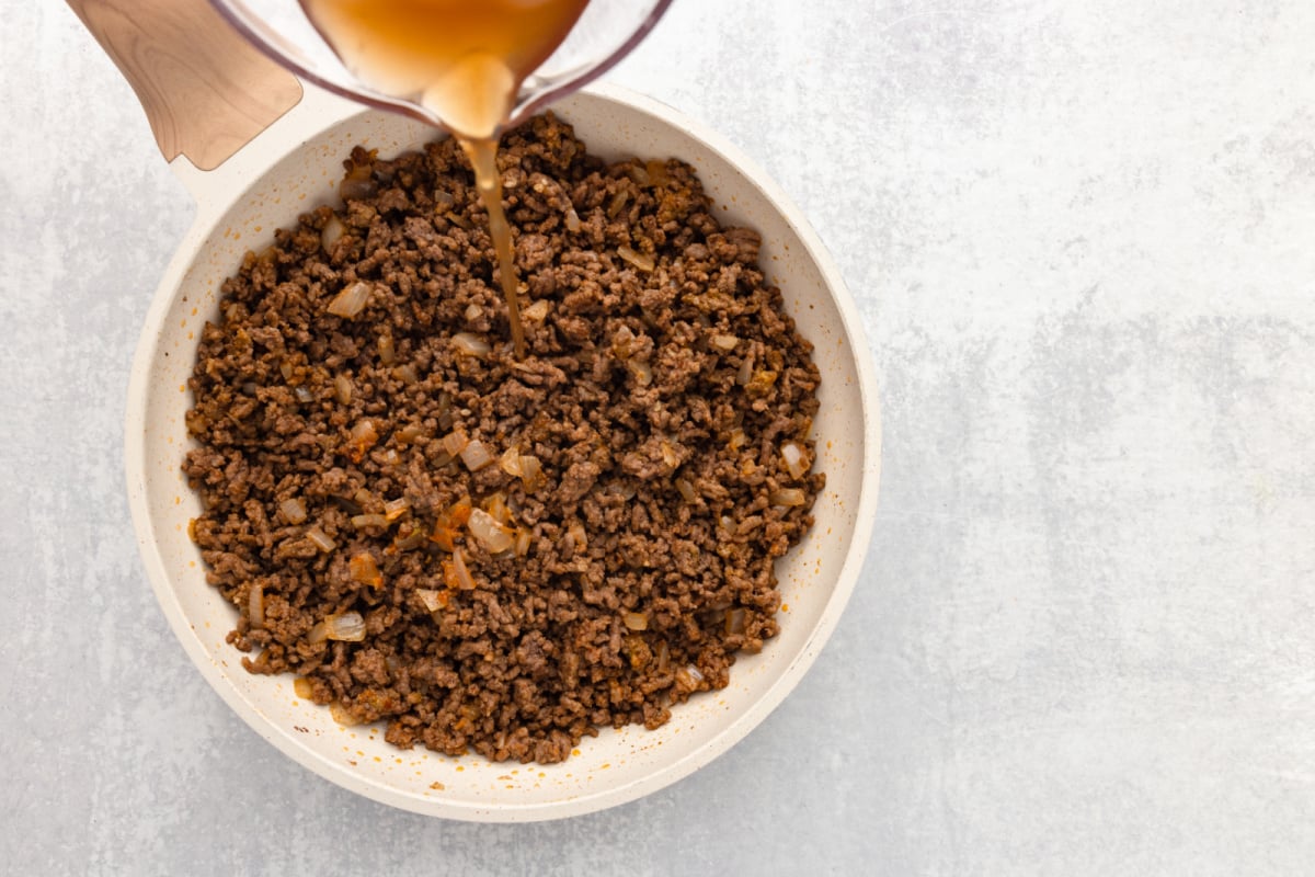 beef broth being added to pan