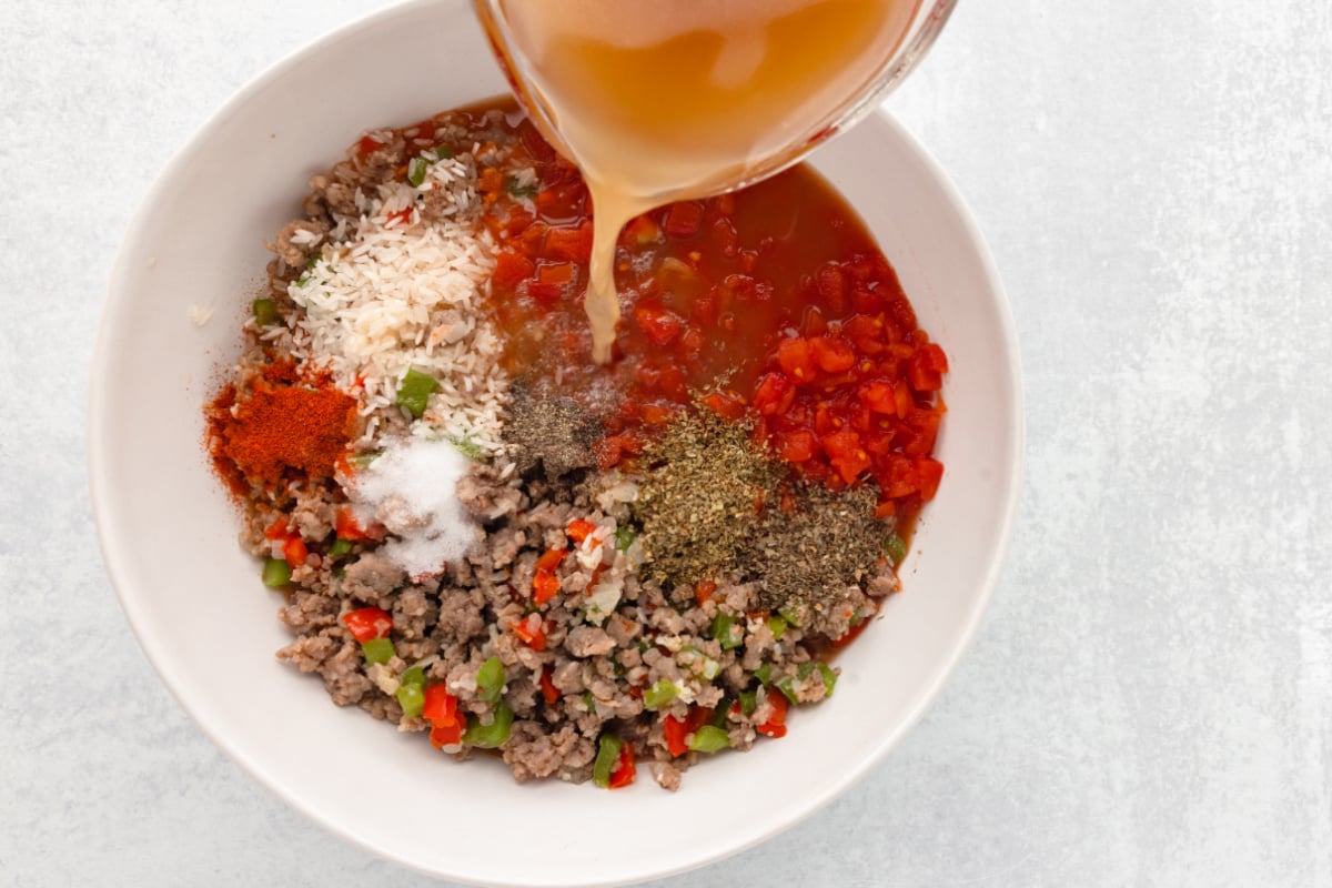 adding broth tomatoes, rice and seasoning in a bowl