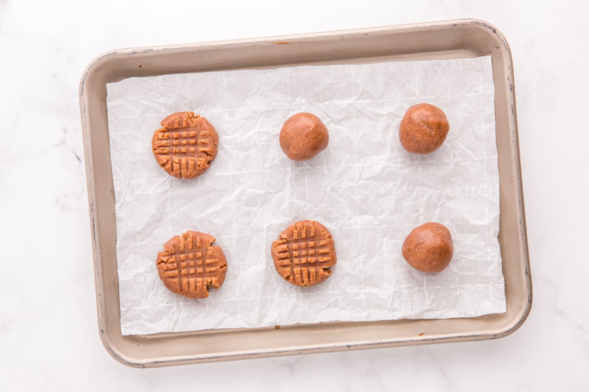 cookie dough balls placed on baking sheet with half flattened with fork