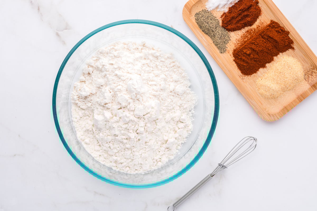 flour, garlic powder, smoked paprika, salt, cayenne pepper and black pepper being mixed into flour