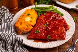maple glazed ham steaks on a plate with potato and green beans