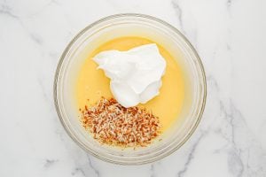 whipped topping and toasted coconut added to a bowl