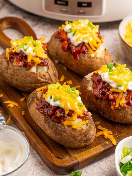 Slow Cooker BBQ Chicken Loaded Baked Potatoes on a cutting board