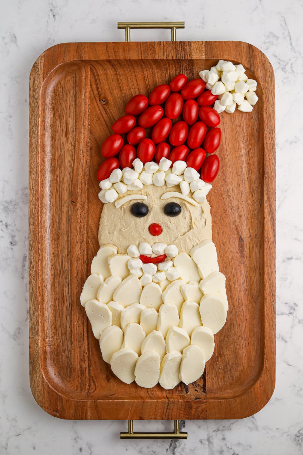 Add cherry tomatoes and mozzarella cheese balls to wooden board to make Christmas hats