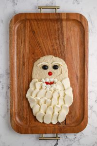 hummus, cheese, black olives, and bell pepper added to board to form Santa face and beard