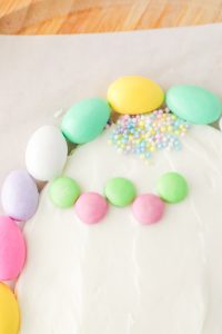adding m&m's to make decorations on frosting egg