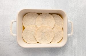 tortillas laid in baking sheet over sauce