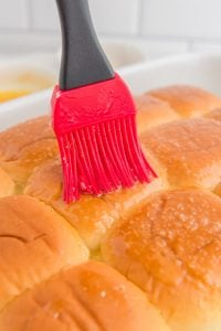 brushing melted butter on top of buns