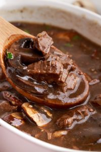 Instant Pot Stewed Beef with Mushroom Gravy in a serving dish with a wooden spoon