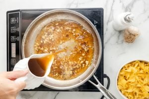 pouring broth into pan with garlic