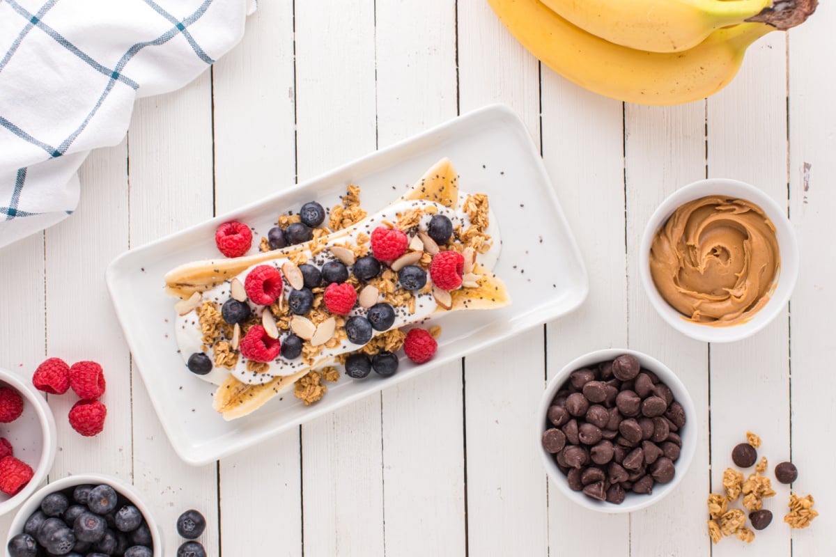 raspberries, blueberries, granola, almond slices, and chia seeds added to top of yogurt and banana