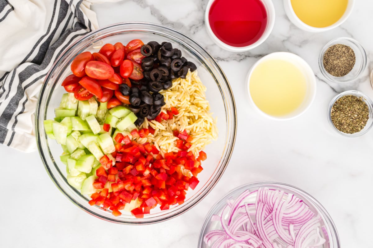 cooked orzo pasta, diced red bell pepper, diced cucumber, halved cherry tomatoes, and sliced black olives in a bowl