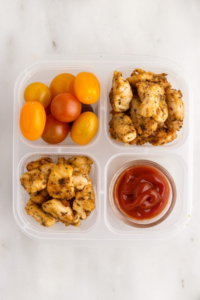 Air Fryer Chicken Bites in a lunchbox with cherry tomatoes and a sauce