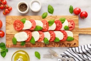 sliced cheese, tomato and basil on a cutting board