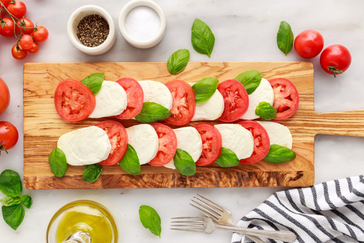 sliced cheese, tomato and basil on a cutting board