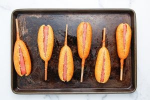 corn dogs slit lengthwise on baking sheet