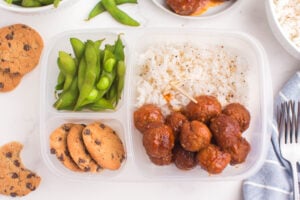 meatballs and rice packed in a lunchbox with cookies and edamame